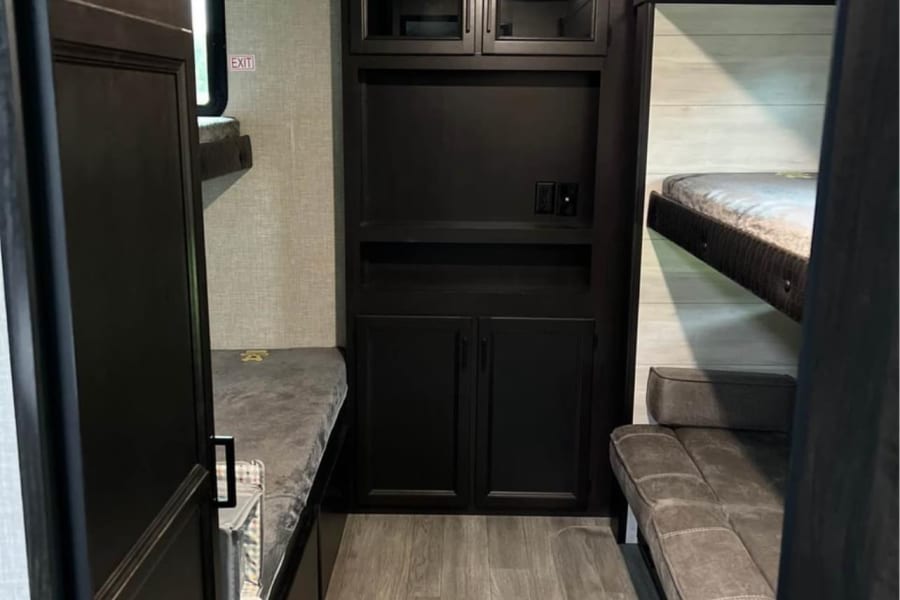 This RV rental features a cozy bunkhouse with multiple sleeping areas, including stacked bunks and a sofa, plus central storage.
