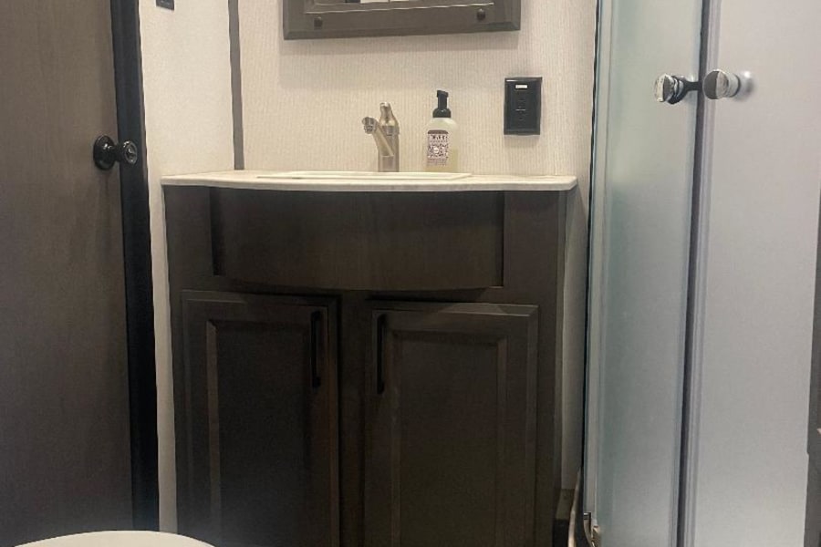 Compact RV rental bathroom with a vanity, toilet, and curved shower, designed for efficient travel.
