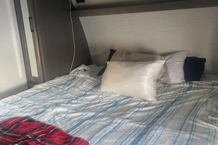 Inside this RV rental bedroom: a comfy bed with blue striped bedding, varied pillows, and compact overhead storage.