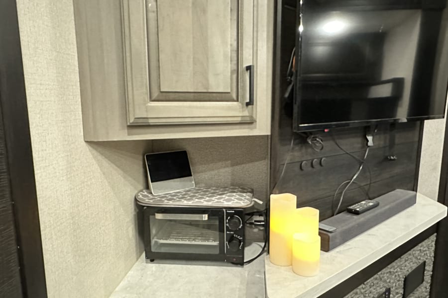 Compact **RV rental** interior: toaster oven, tablet, TV, and soundbar create a cozy living space.