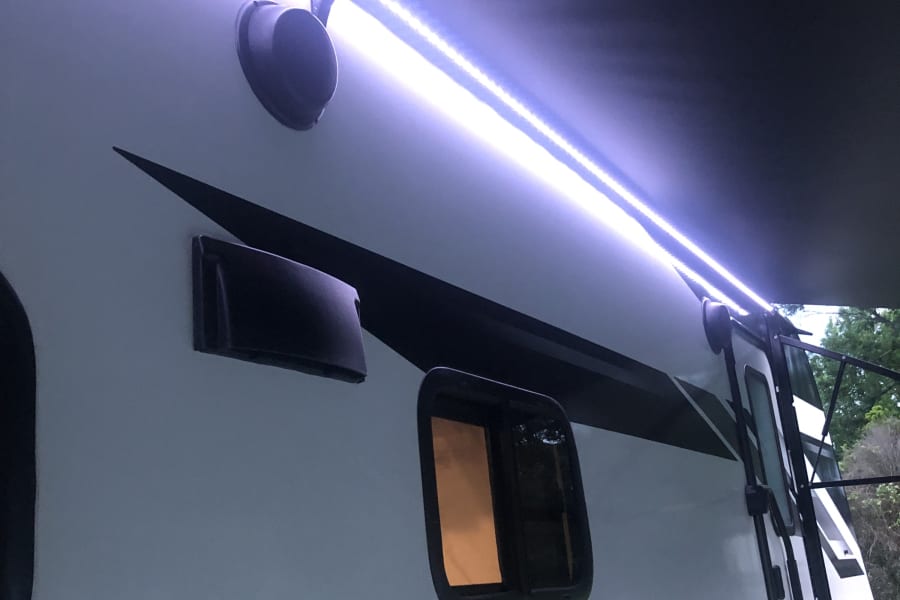 Night view of a Grand Design Imagine RV rental with bright LED awning lights, perfect for camping.