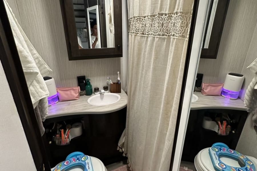 RV rental bathroom with toilet, child's potty seat, vanity, sink, and shower. A mirror reflects the interior.