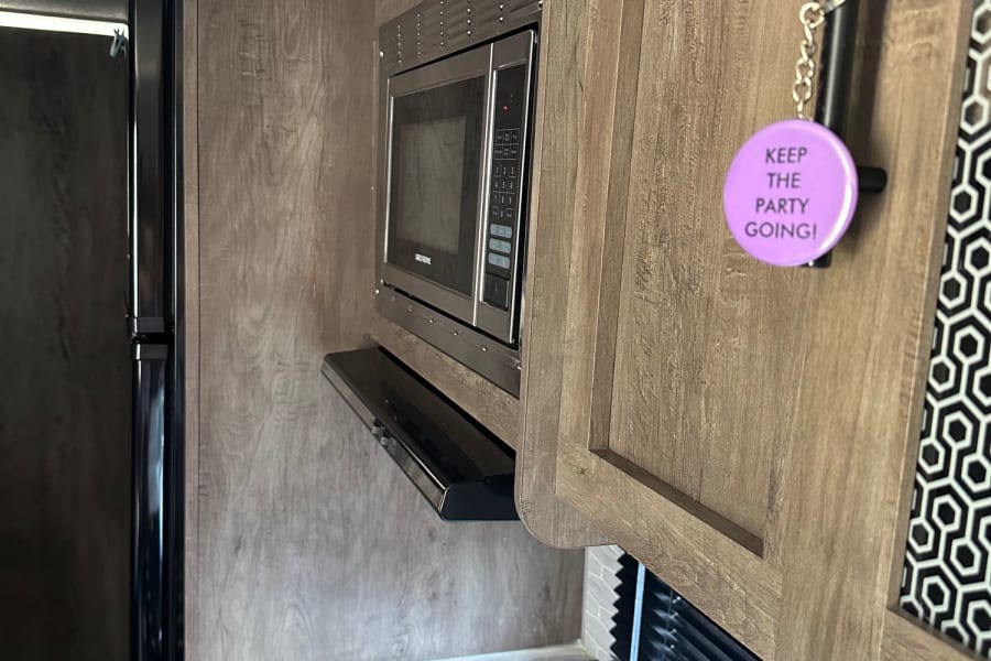 Compact rv rental kitchen. Features microwave, stovetop, fridge, wood cabinets, and a fun "Keep the Party Going!" keychain.