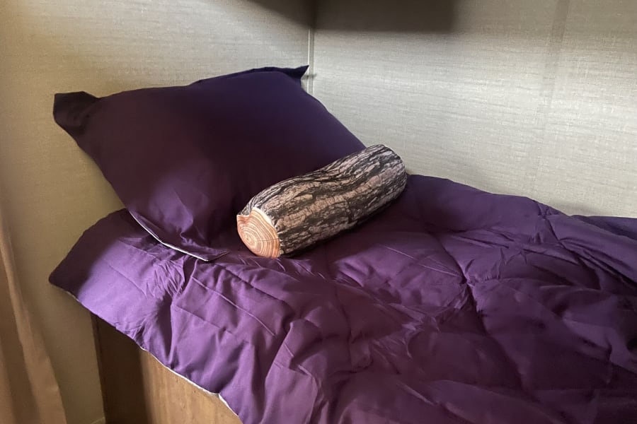 Cozy purple bed with a log pillow in an RV rental, offering comfortable sleeping for your travels.