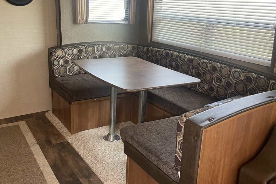 RV rental interior: cozy dinette with U-shaped seating, table, and windows with blinds.