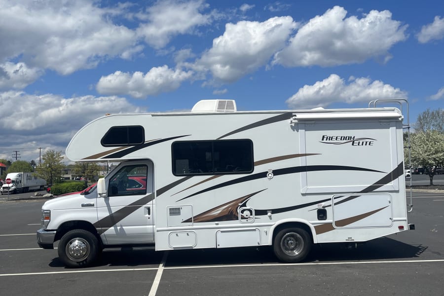 White Freedom Elite RV rental parked in a sunny lot with blue sky and white clouds. Perfect for your next trip.