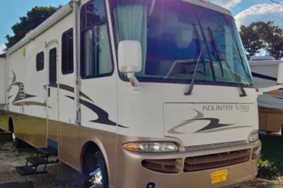 A large, two-tone (white and tan) Kountry Star motorhome for rv rental, parked on a sunny day.