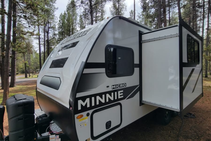 Modern Minnie Micro RV rental set in a peaceful pine forest campground. Features a slide-out for more room.
