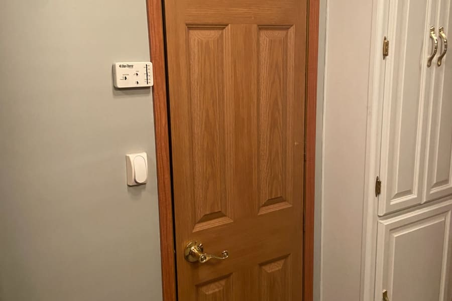 Inside an RV rental: a wooden door with an over-door hook rack, climate control thermostat, and built-in white cabinets.