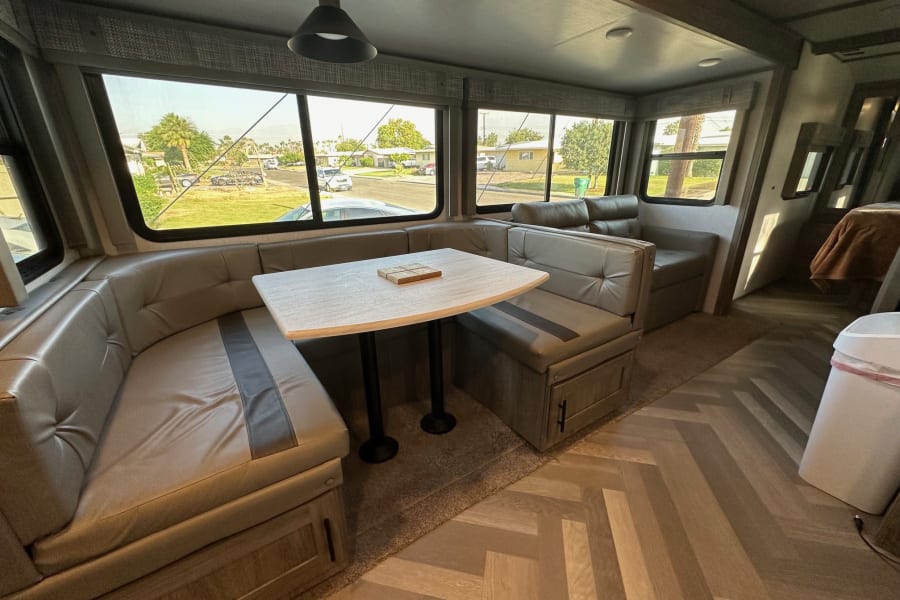 Inside your RV rental: a modern, spacious dinette with cozy seating, a dining table, and large windows revealing a neighborhood view.