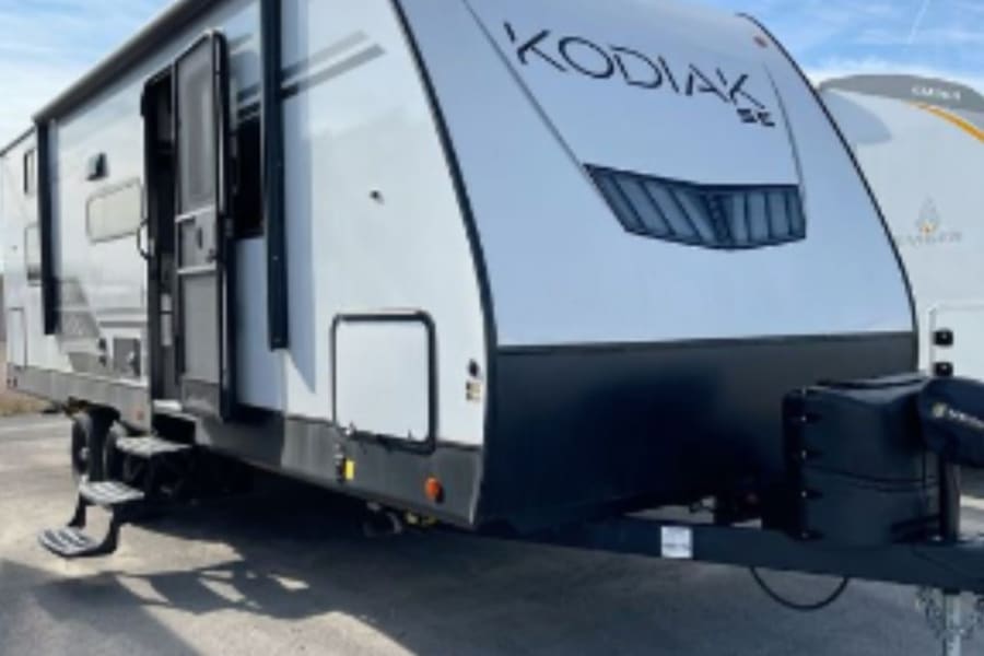 "KODIAK SE" travel trailer, a spacious white RV for rental. Features include an extended entry door and steps, ideal for outdoor recreation.