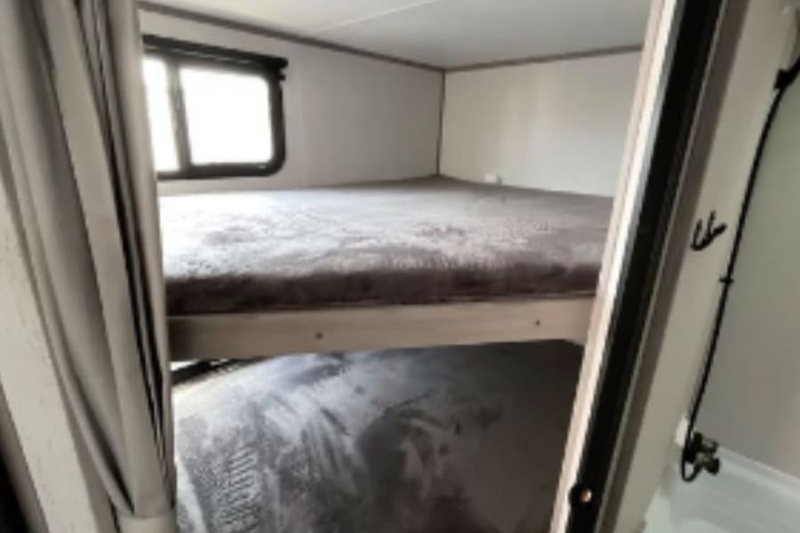 Cozy RV rental interior with bunk beds, soft grey blankets, a window, and a compact bathroom section visible.