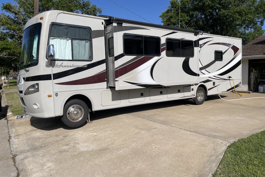 Cream-colored Hurricane RV rental motorhome parked on concrete driveway with side expanded.