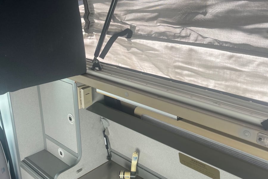 Compact RV rental camper van kitchen area with sink, cabinets, and a raised pop-top roof for added space.
