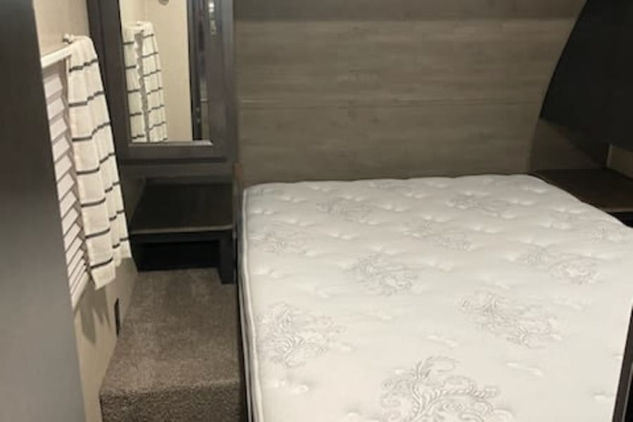 Cozy RV rental bedroom with a comfy bed, overhead cabinets, and a mirror. Perfect for your next adventure!