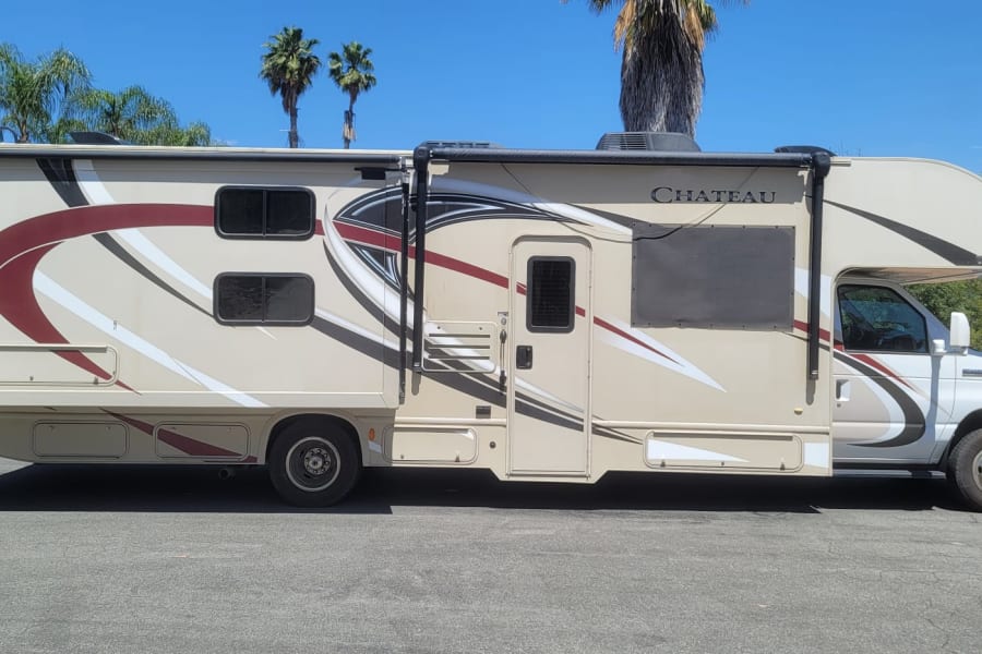 Side view of a tan and maroon Class C RV rental, parked outdoors on a clear day. Ready for your next road trip!