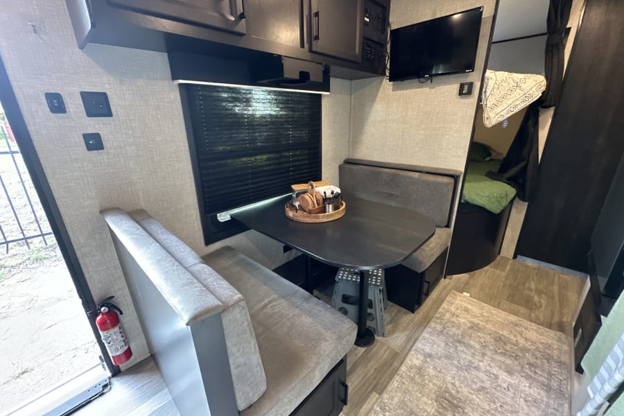 Spacious RV rental interior featuring a modern dinette, TV, and cozy sleeping area, ideal for travel adventures.