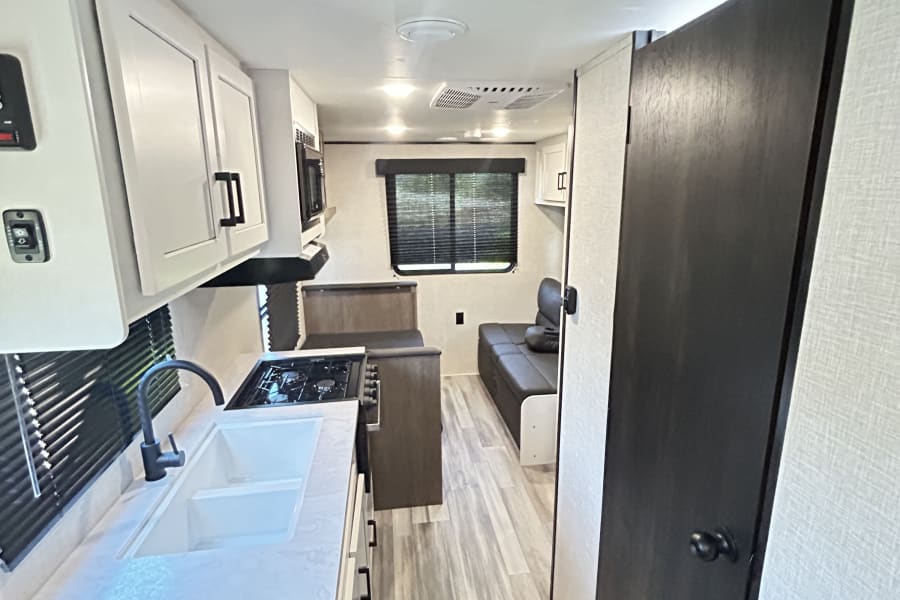 Clean RV rental interior featuring a bright kitchen with double sink & stovetop, ample storage, and comfy dinette seating.