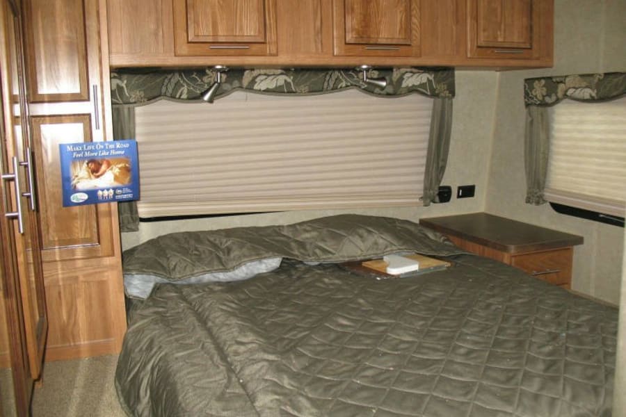 Cozy RV rental bedroom: large bed with quilted comforter, wood cabinets, and windows, making travel feel like home.