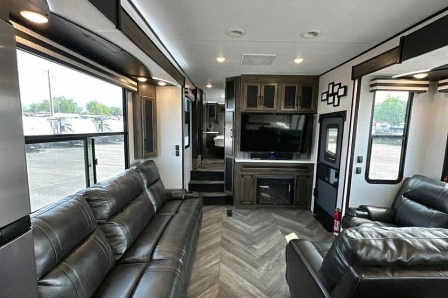 Spacious RV rental interior: features comfortable black leather seating, large windows, and a modern entertainment center.