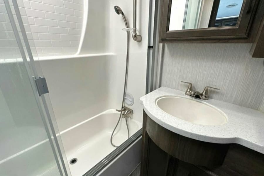 This RV rental bathroom offers a shower-tub combo with glass doors, a vanity with sink, and a mirrored cabinet, maximizing space.
