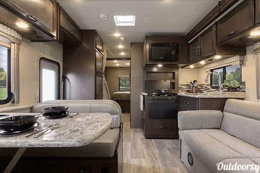 Explore this modern RV rental's interior: a full kitchen, comfy dinette, living area with sofa, and rear bedroom.