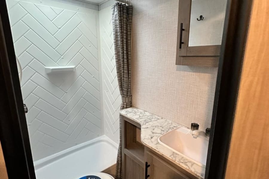 Inside an RV rental: a compact bathroom with a shower (herringbone walls), a toilet (Camping World sticker), and a vanity sink.