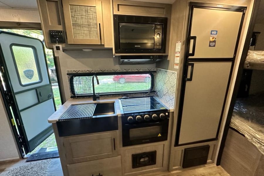 RV rental interior: compact kitchen with sink, stove, microwave, fridge, and bunk beds. Exit door visible.