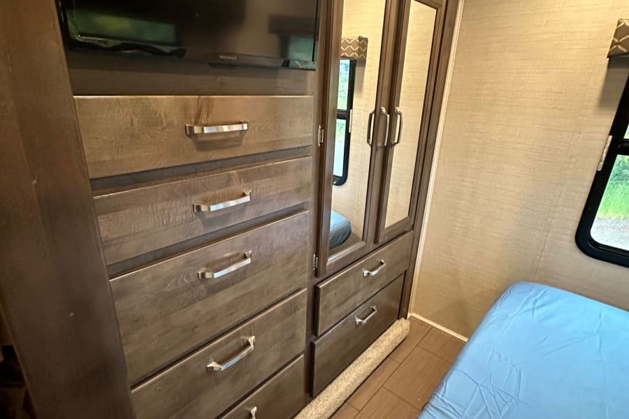 RV rental bedroom with wood dresser, TV, mirrored closet, and light blue bed.