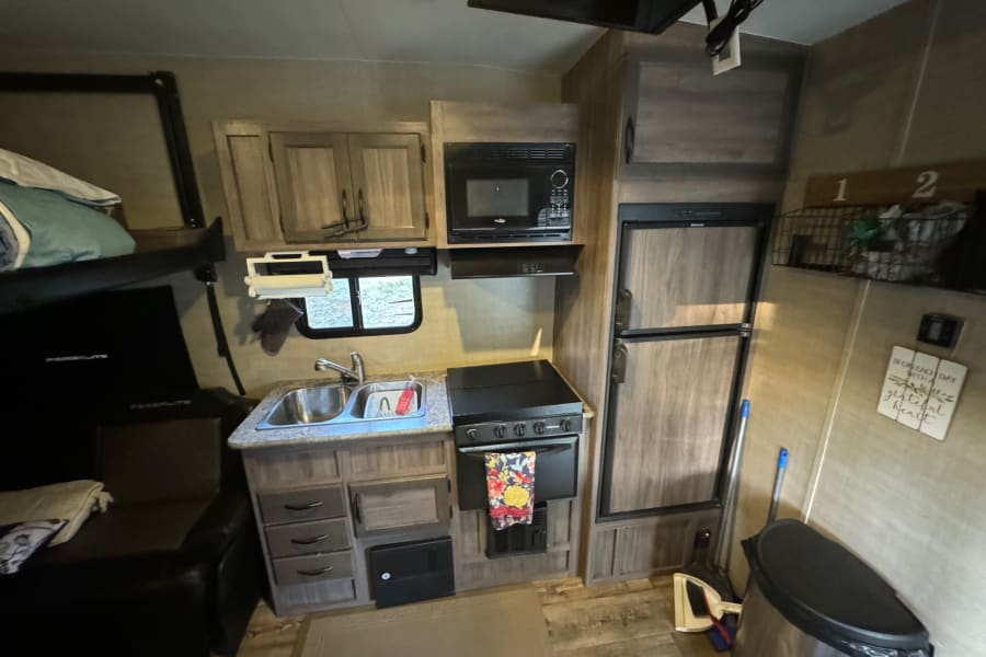 RV rental interior showcasing a compact kitchen with a stove, microwave, fridge, and cozy bunk beds.