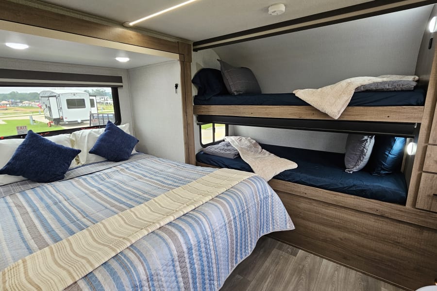 This RV rental offers a cozy main bed with blue bedding and stacked bunk beds, providing comfortable travel accommodations.