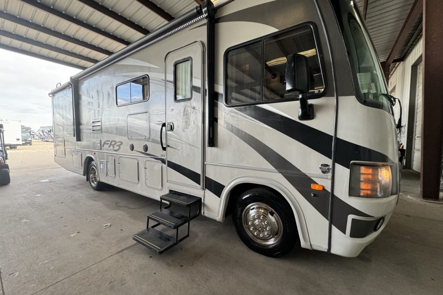 RV rental: A large white and gray motorhome parked under a metal roof, with its entrance steps open.