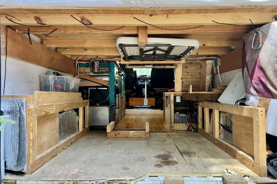 Rear interior of a DIY van conversion, ideal for an RV rental. Features rustic wood framing, storage, and an overhead table.