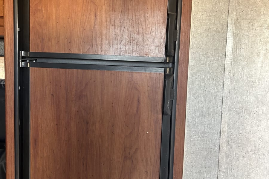 Interior view of an RV rental refrigerator, featuring wood-look doors and top Dometic controls.