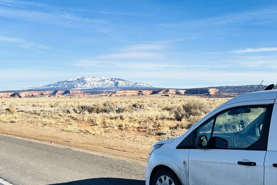 White RV rental van stopped on a road, overlooking a desert landscape with distant snow-capped mountains.
