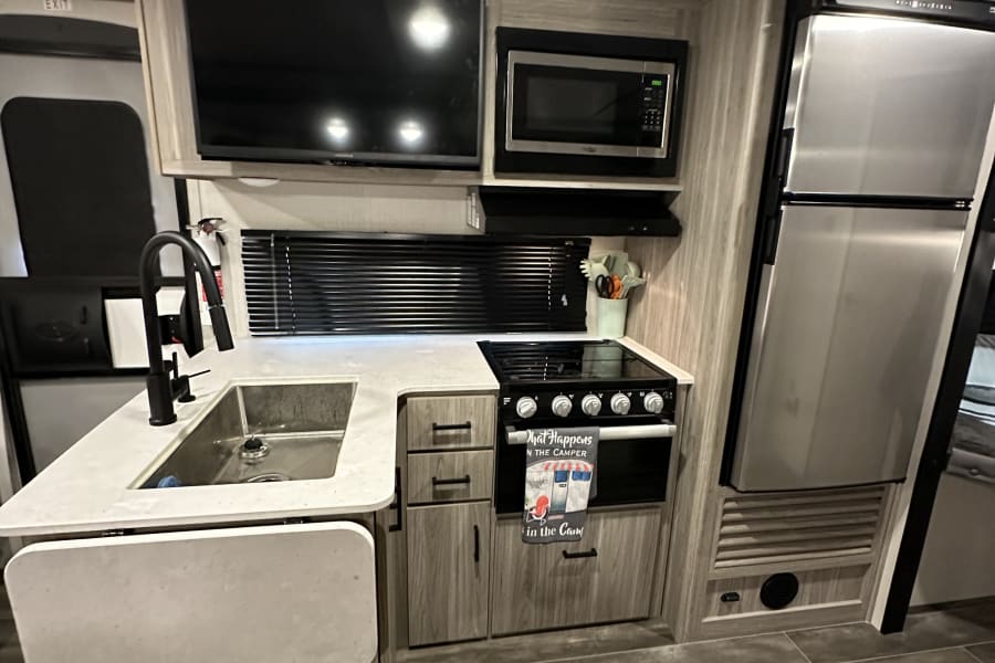 A well-appointed RV rental kitchen with a sink, stove, microwave, and fridge, efficiently designed for comfortable living.