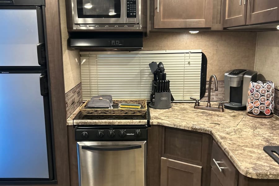 Modern RV rental kitchen with stainless steel appliances: fridge, microwave, oven, sink. Compact & functional.