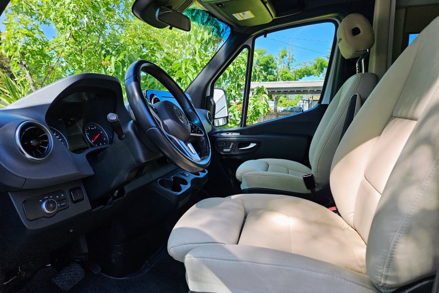 Step into your RV rental: a bright Mercedes-Benz van cabin. Light-colored front seats, black dashboard, and steering wheel visible.