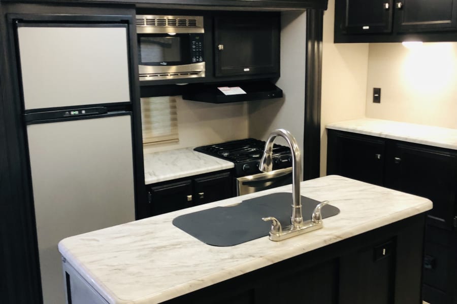 Modern RV rental kitchen with black cabinets, marble-look counters, and stainless steel appliances, including an island sink.
