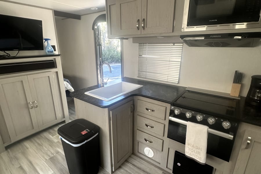 Modern RV rental kitchen with stove, microwave, sink, and TV. Bright, compact interior space.