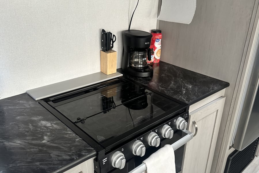 RV rental kitchen with black stove/hood, microwave, coffee maker, and dark counters. Light cabinets & paper towels.