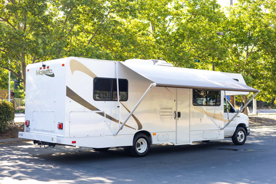 White Majestic Class C RV rental, awning extended, parked outdoors. Ideal for trips and adventures.