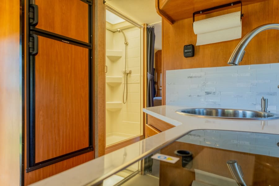 This RV rental's compact interior includes a kitchen with sink, Dometic fridge, and a functional shower, perfect for your adventures.