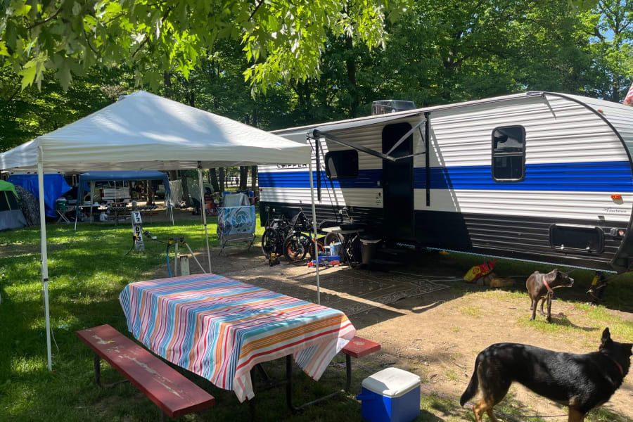 Sunny campsite with an RV rental, tent, picnic table, and two dogs, perfect for outdoor camping adventures.