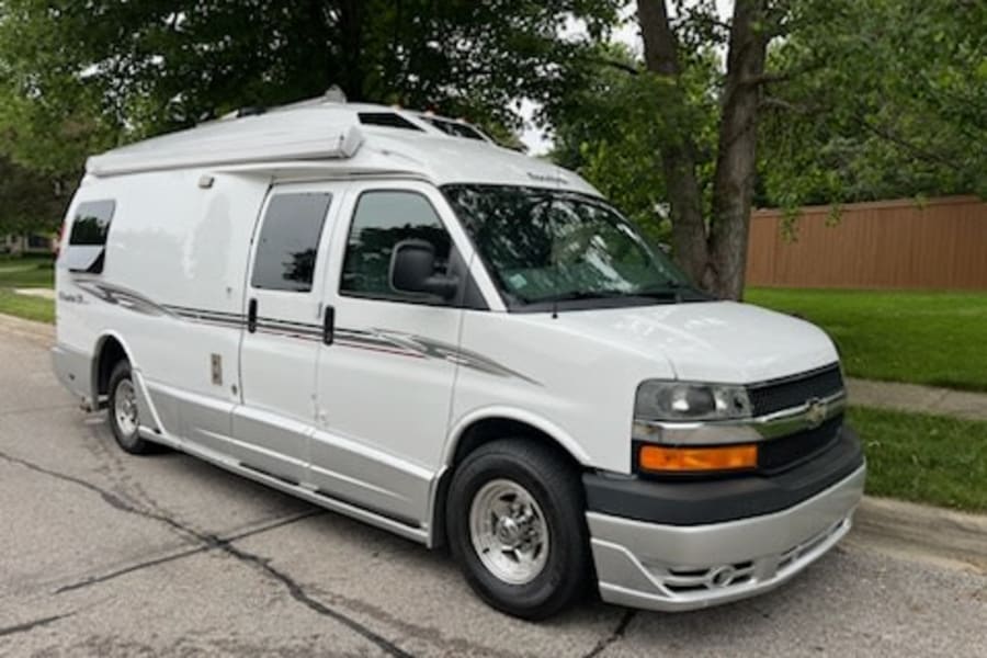 This white Chevrolet Express RV rental, featuring a raised roof and side awning, is perfect for your next campervan adventure.