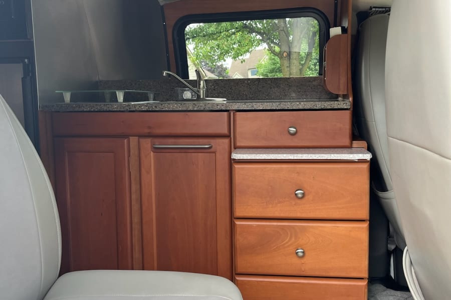 Inside an RV rental: a cozy kitchen with sink, wood cabinets, microwave, and outdoor view.