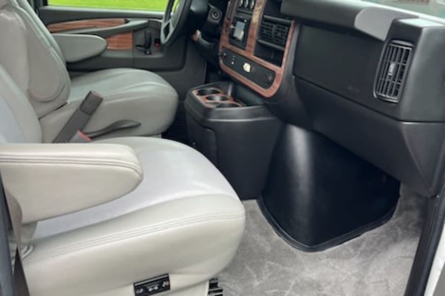 Explore the front interior of this RV rental, featuring comfortable captain's chairs, a wood-grain dashboard, and carpeted floor.
