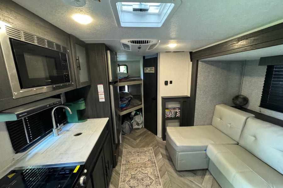 This RV rental's interior offers a compact kitchen, living area with sofa, and bunk beds, perfect for travel comfort.