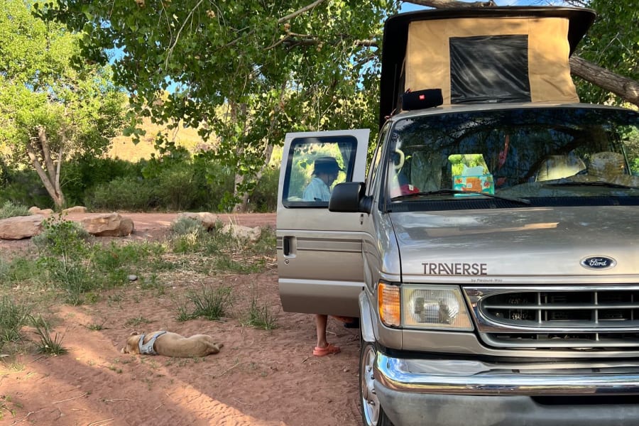 A Ford Traverse camper van (RV rental) under trees, dog naps on red earth. Ideal van life camping adventure.