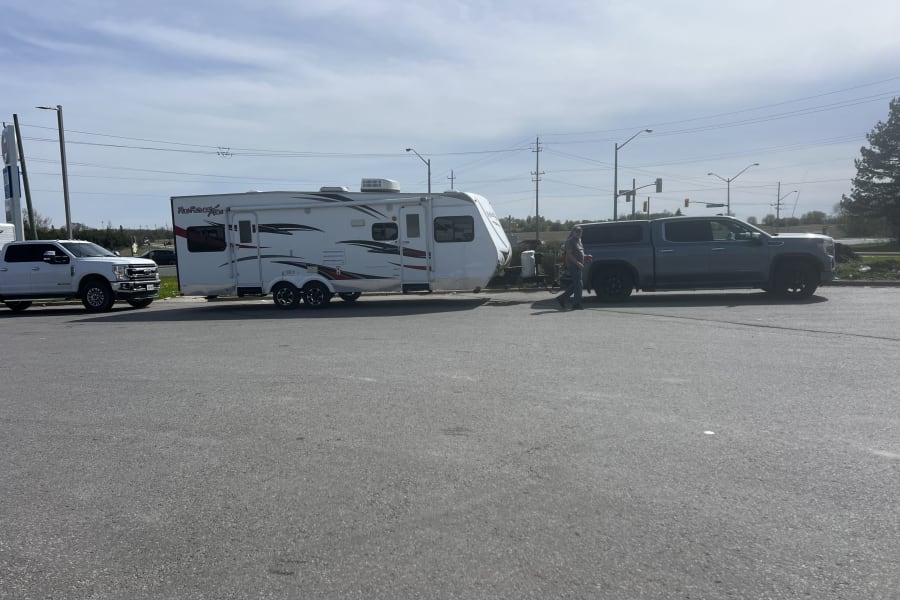 A white travel trailer, possibly an rv rental, is hitched to a grey pickup truck.